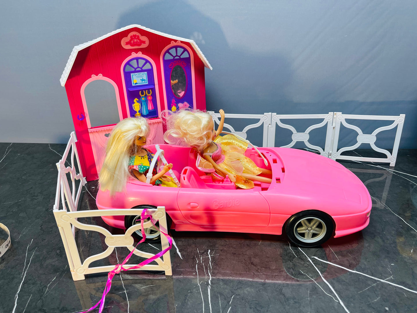 Barbie Glam Convertible car along with two Barbie dolls and a small playhouse.