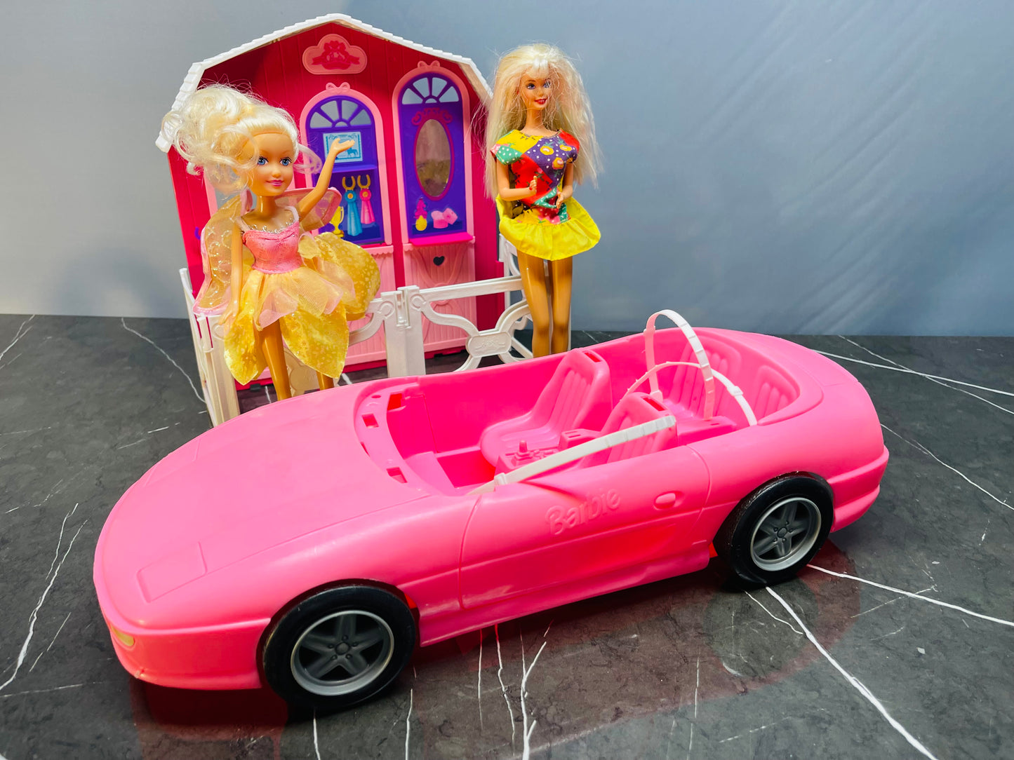Barbie Glam Convertible car along with two Barbie dolls and a small playhouse.
